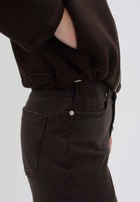 Pantalon en denim noir avec poches latérales et finitions en métal argenté. Assorti à un sweat-shirt sombre avec cordon de serrage à la taille et poignets côtelés.