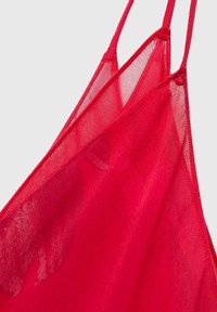 Camisole en tissu transparent rouge avec des bretelles fines, une texture délicate et un design drapé mettant en valeur un jeu subtil de lumière à travers le matériau.
