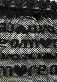 Zwarte kant stof met een hexagonaal patroon, met tekst en hartvormen. Een klein zwart hartje is bevestigd aan de bovenrand.