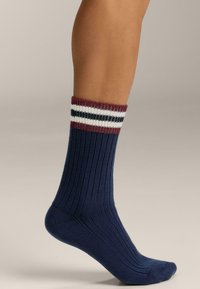 Calzini blu navy a coste con un design testurizzato, caratterizzati da un bordo a righe bordeaux, bianco e blu navy. Il tessuto appare liscio ed elastico.