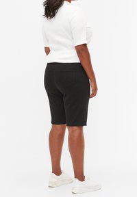 Pantalones cortos de mezclilla negra con cintura a media altura, que incluyen dos bolsillos traseros, combinados con una camiseta blanca ajustada y zapatillas blancas.