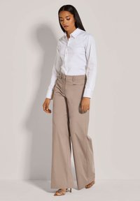 Witte overhemden met lange mouwen gecombineerd met lichtbeige wijde broek. De outfit heeft een schoon ontwerp en een gladde textuur.