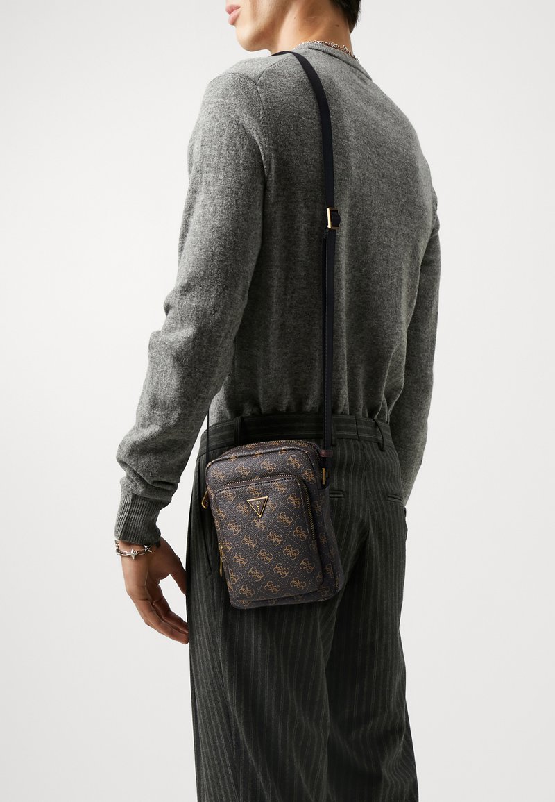 Sac bandoulière marron foncé avec motif logo doré, en cuir, poche zippée, bandoulière réglable et forme rectangulaire. Surface texturée.