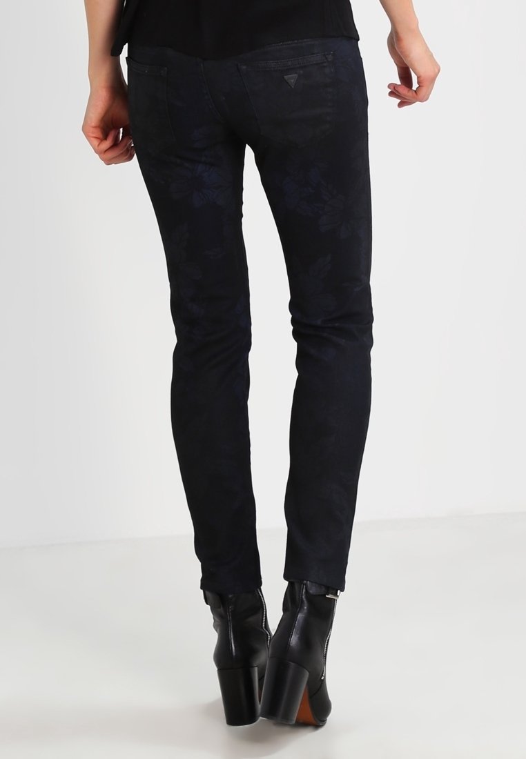 Jeans ajustados de estampado floral negro con una textura suave, que cuentan con bolsillos traseros y se combinan con botas de tacón negro hasta el tobillo.