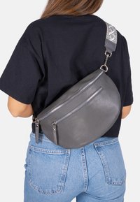 Sac bandoulière en cuir gris avec une finition texturée, présentant une forme incurvée, deux poches zippées et une bandoulière décorative.