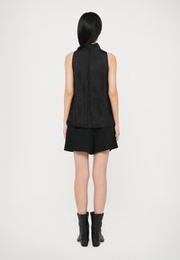 Zwarte mouwloze top met hoge hals en ritssluiting. Gecombineerd met losse zwarte shorts en enkellaarzen. Soepele textuur en minimalistisch ontwerp.