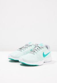 Scarpe da ginnastica verde chiaro con texture a righe, dettagli grigi e il logo Nike in turchese. Costruzione leggera e suola bianca.