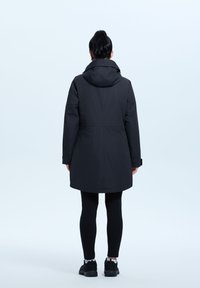 Giacca nera con cappuccio, chiusura con zip e bottone, leggermente svasata in vita, in tessuto strutturato e che arriva a metà coscia.