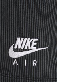 Černá ribovaná tkanina má bílé vyšívané logo "NIKE AIR" s designem swoosh. Zaměření na texturu a jasnost loga.