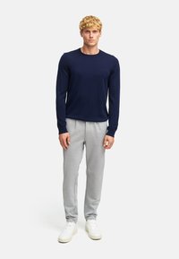 Maglione a girocollo lavorato a maglia di colore navy abbinato a pantaloni della tuta grigi chiari e sneakers bianche. L'outfit presenta una vestibilità comoda e tessuti morbidi.