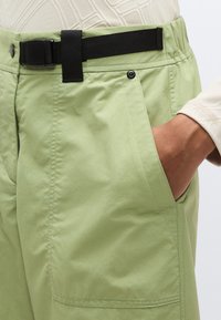 Φωτεινό πράσινο παντελόνι με υφή υφάσματος, διαθέτει μαύρη ρυθμιζόμενη ζώνη, πλαϊνές τσέπες και σχέδιο με άνετη εφαρμογή.