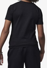 Black cotton T-shirt with short sleeves and a crew neck. Smooth texture and relaxed fit, paired with matching black pants.