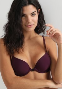 Soutien-gorge mauve rembourré avec des bretelles fines ajustables, texture lisse et fermeture à crochet à l'arrière. Design simple avec un léger éclat.