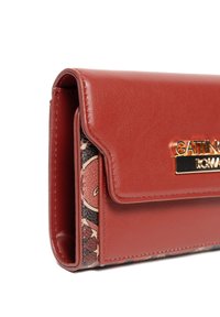 Rode neplederen portemonnee met een klepafsluiting, voorzien van een gouden logo-plaque, en een getextureerde stoffen patroon dat aan de zijkant zichtbaar is.