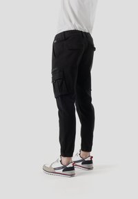 Pantalones cargo negros con cinturilla elástica, piernas ajustadas y múltiples bolsillos laterales, combinados con zapatillas grises y blancas.
