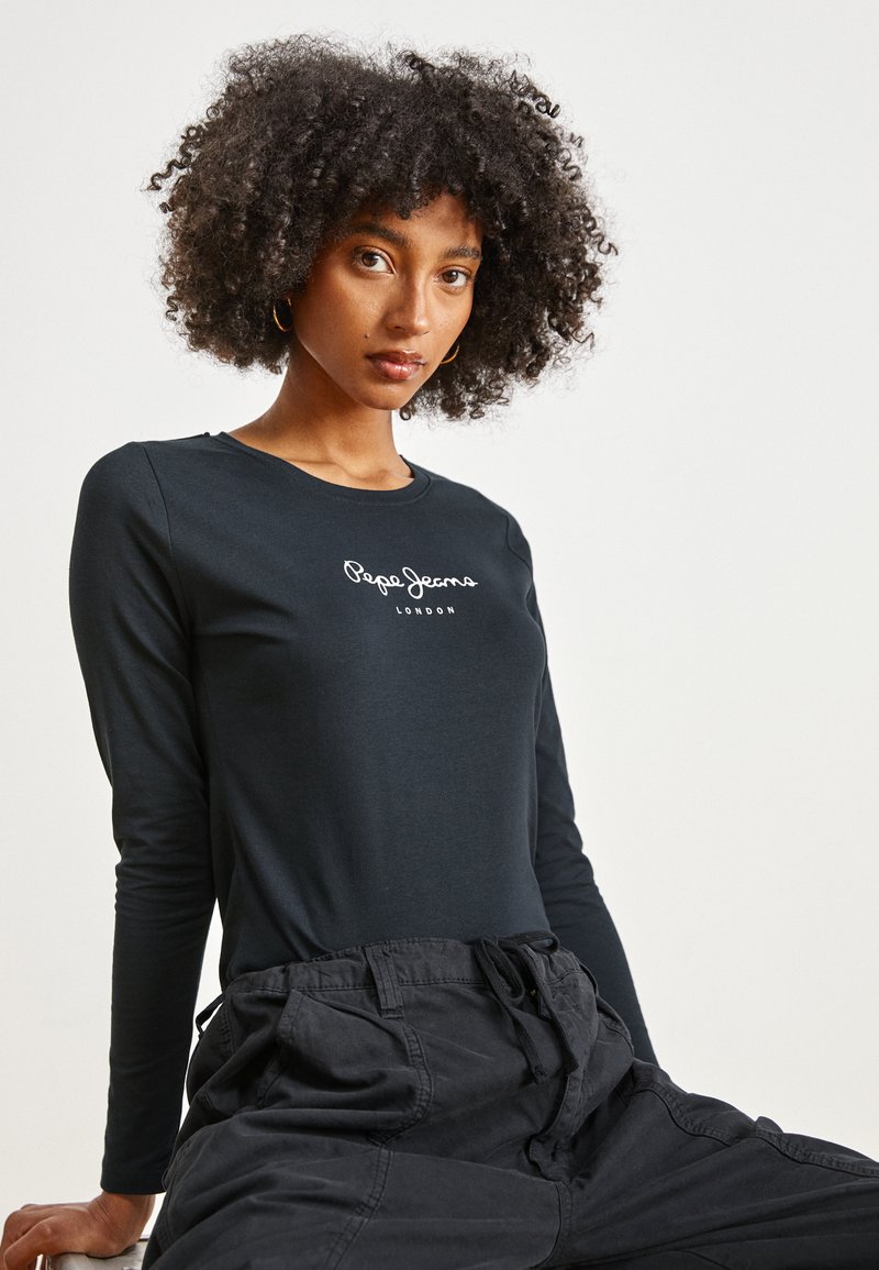 Juodas ilgomis rankovėmis marškinėliai su balta "Pepe Jeans London" logotipu, derinami su laisvomis juodomis kelnėmis. Lygus audinio tekstūra, minimalistinis dizainas.