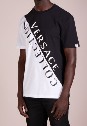 Czarny i biały T-shirt z ukośnym podziałem. Na czarnej stronie znajduje się napis "VERSACE COLLECTION" w wyraźnym, odbijającym świetle kolorze.