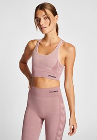Ljust rosa sportbh och leggings-set, med en texturerad yta, och Hummel-logotyp. Designen inkluderar en subtil chevronmönster längs sidorna.