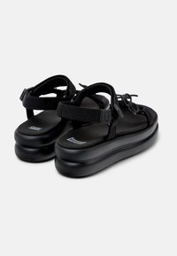 Sorte sandaler med justerbare stropper, en polstret svart såle og en plattformdesign for ekstra høyde og komfort.