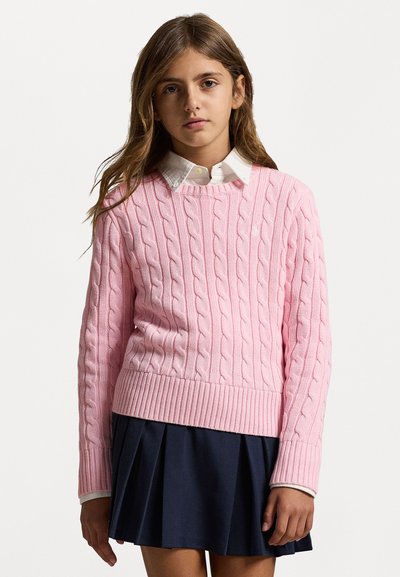 Ροζ πλεκτό πουλόβερ με ριγωτό στρίφωμα, φορεμένο πάνω από ένα λευκό πουκάμισο με γιακά. Συνδυάζεται με μια ναυτική πτυχωτή φούστα. Μαλακή υφή και άνετη εφαρμογή.