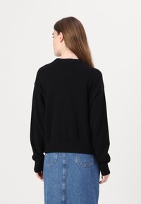 Črna pletena jopica s krožnim izrezom, spušenimi rameni in ribjim robom. V kombinaciji z modrim jeans krilom, vidnimi šivi.