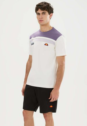 Jonge man staand, draagt een wit en paars kortemouwen T-shirt en zwarte short met bijpassende oranje logopatches op T-shirt en short.