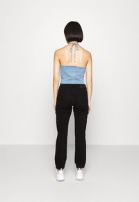 Denim halter top in light blue, paired with black cargo pants. The outfit features a fitted silhouette and a tie at the back neckline.
