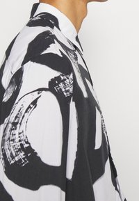 Kariertes Hemd in Schwarz und Weiß mit abstrakten Kreis Mustern; aus leichtem Stoff mit glatter Textur; klassischer Kragen.