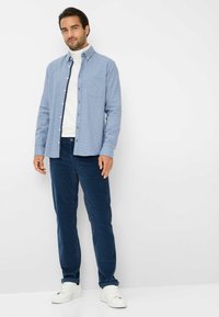 Lichtblauw button-up shirt met een gestructureerd patroon, gecombineerd met marineblauwe corduroy broeken en witte sneakers. Eenvoudig ontwerp met een borstzak.