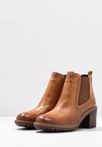 Braune Leder-Stiefeletten mit einer abgerundeten Spitze, elastischen seitlichen Einsätzen und einem stabilen Blockabsatz. Strukturiertes Gummisohlenprofil für guten Halt.