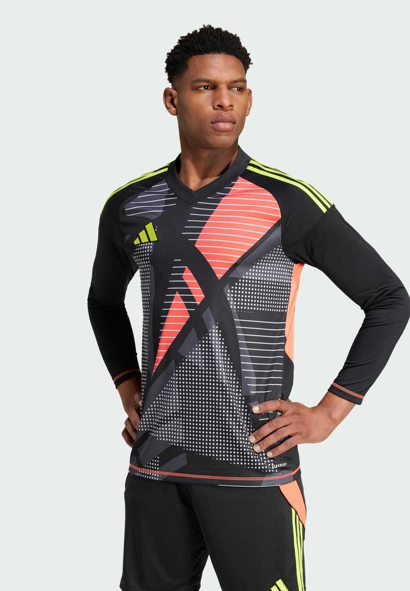 Uomo che indossa una maglia sportiva nera con motivi geometrici arancioni, grigi e giallo neon, abbinata a pantaloni corti neri con bande giallo neon.