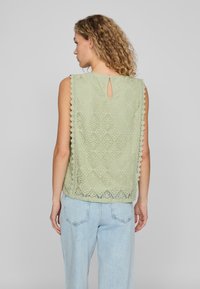 Top in pizzo verde chiaro con orlo a merletto, chiusura a stipite sul retro e motivo floreale. Abbinato a jeans blu chiaro a vestibilità ampia.
