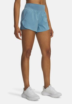 Pantalones cortos deportivos de color azul claro con una cinturilla elástica amplia, textura suave y aberturas laterales para mayor libertad de movimiento, combinados con zapatillas blancas.