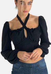 Zwart langarmig topje met een diepe halslijn. Voorzien van gerimpelde randen en gekruiste bandjes. Gladde textuur, aansluitende pasvorm.