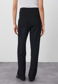 Pantaloni neri slim-fit con una texture liscia e una vita alta. La parte posteriore presenta due tasche e un taglio dritto fino alle caviglie.