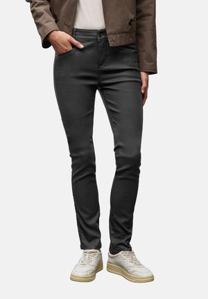 Jeans ajustados negros de tejido suave, con bolsillos frontales y cremallera, combinados con zapatillas de color claro y una camiseta en tonos neutros.