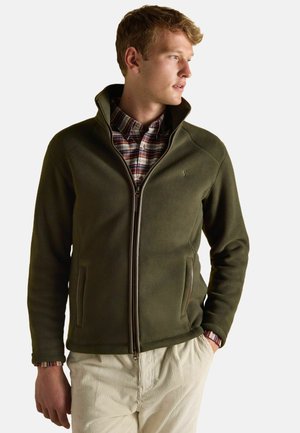 Olive green fleece jacket with a high collar, zippered front, and pockets. Worn over a plaid shirt, featuring ribbed sleeve cuffs.