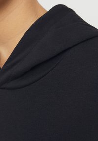 Čierna mikina s kapucňou, vyrobená z mäkkej struktúrovanej látky, s okrúhlou kapucňou. Látka má rebrovaný vzor pri výstrihu.