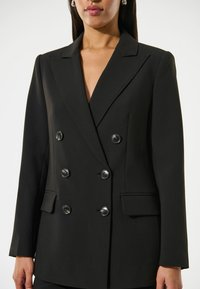 Blazer nero doppiopetto realizzato in tessuto liscio, con rever a punta, due tasche frontali e bottoni lucidi per la chiusura.