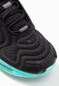 Černá sportovní obuv s texturovanou tkaninou, vlnitým designem, šedými tkaničkami a tyrkysovou podrážkou. Na botě je výrazné černé logo Nike.