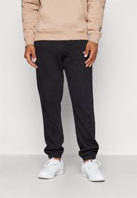Schwarze Jogginghosen aus weichem Material mit einem elastischen Bund, gerippten Knöcheln und einem kleinen gestickten Logo am linken Oberschenkel.