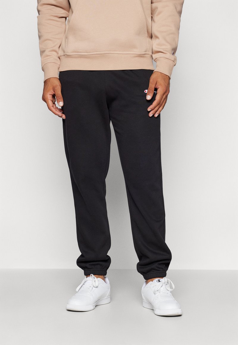 Schwarze Jogginghosen aus weichem Material mit einem elastischen Bund, gerippten Knöcheln und einem kleinen gestickten Logo am linken Oberschenkel.