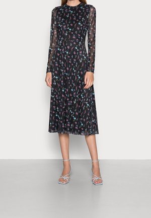 Zwarte midi-jurk met doorschijnende lange mouwen en een meerkleurige kleine bloemprint, gecombineerd met lichtblauwe sandaaltjes met hak en bandjes.