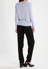 Maglione azzurro chiaro a maglia con scollatura ampia e cucitura posteriore, abbinato a pantaloni neri comodi e tacchi neri.