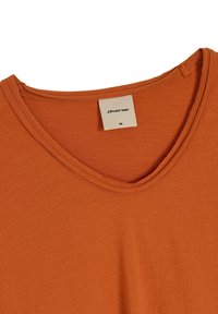 Pomarańczowa koszulka z krótkim rękawem z dekoltem w serek. Wykonana z lekkiego, teksturowanego materiału. Zawiera metkę z napisem "diverse" oraz rozmiar "M."