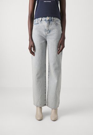 Jeans a vita alta e gamba larga in denim azzurro chiaro. Presentano un classico design a cinque tasche e una leggera sfumatura. Abbinati a stivali béige con tacco.