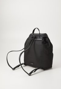 Mochila negra hecha de nailon con acentos de cuero. Cuenta con correas ajustables y un asa en la parte superior. Diseño minimalista con una placa de logo.