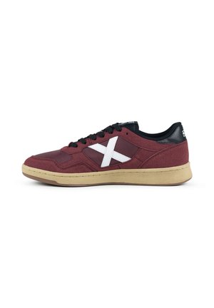 Zapatilla baja de color granate con cordones negros, logo blanco de cruz lateral, cuello de talón negro y suela de goma beige.