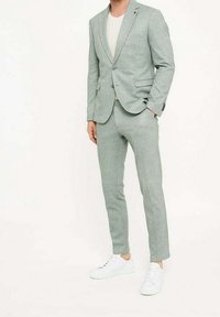 Jasnozielony garnitur z fakturowanej tkaniny, zawierający dopasowaną marynarkę, zwężane spodnie oraz białe trampki dla nowoczesnego wyglądu.