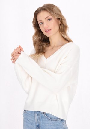 Maglione a V con maniche lunghe in morbido knit bianco. Presenta una vestibilità rilassata con polsini e orlo a costine, abbinato a jeans azzurri.